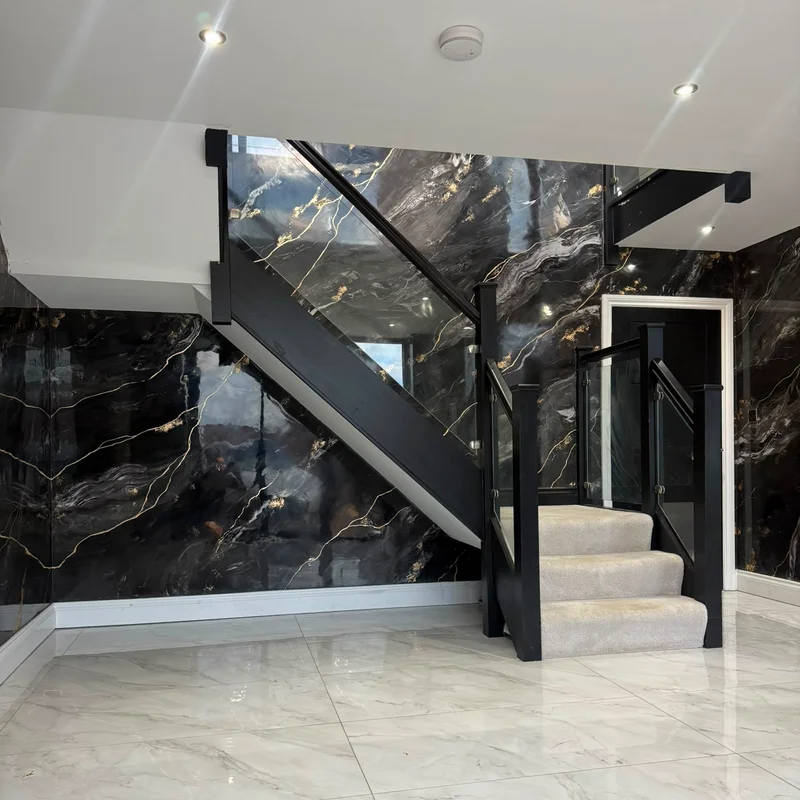 Hallway and staircase walls in high-gloss black marble-effect Venetian plaster with gold veins and gold leaf, beside a black staircase with glass balustrade