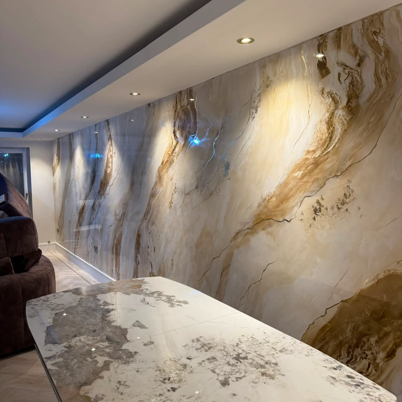 A long living room feature wall in cream marble-effect Venetian plaster with sweeping gold and bronze veins, lit by downlights