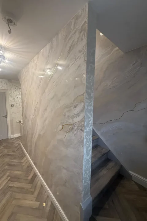 Hallway and stairwell walls in polished white and grey marble-effect Venetian plaster with fine gold veins, catching the light from the ceiling