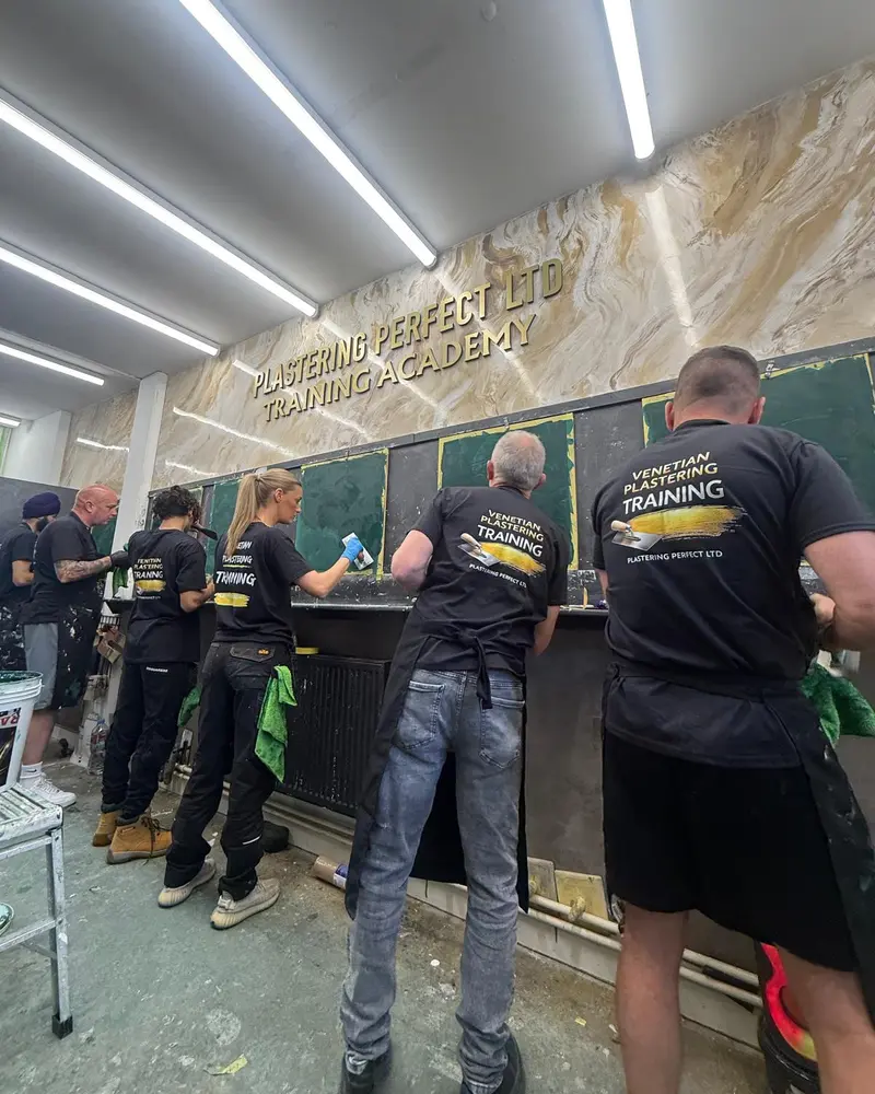 Trainees in Plastering Perfect Training t-shirts applying Venetian plaster to practice wall panels in the training academy.